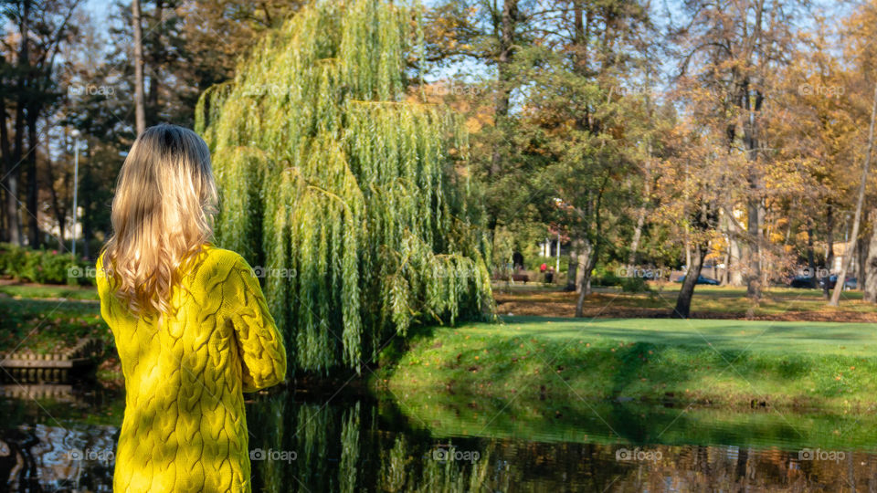 A young, beautiful, blonde woman walking through the autumn park and rejoice in colorful tree leaves.