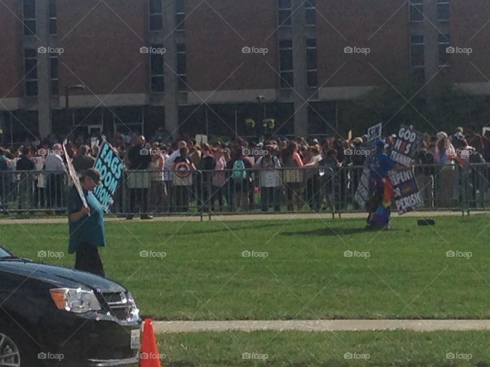 Westboro Baptist church members holding signs to protest an LGB club formed by students of IUPUI. Club supporters and spectators stand in the background behind the fence.