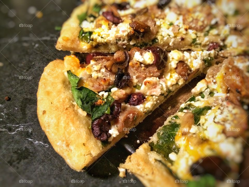 Delicious Mediterranean Pizza featuring Feta Cheese, Spinach, Sausage, Olives, Garlic, Mushrooms and Olive Oil.