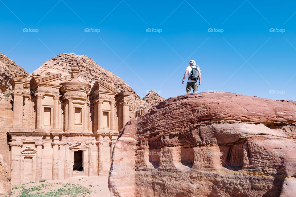 Low angle view of a traveler on a rock while looking towards the ancient monastery of Petra, Jordan