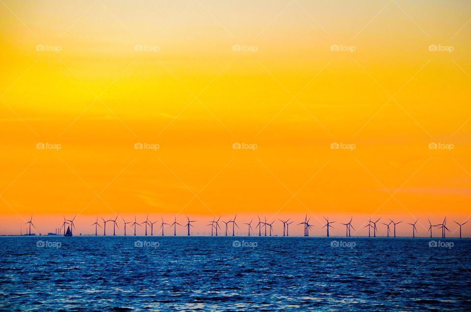View of sea with wind turbine against dramatic sky