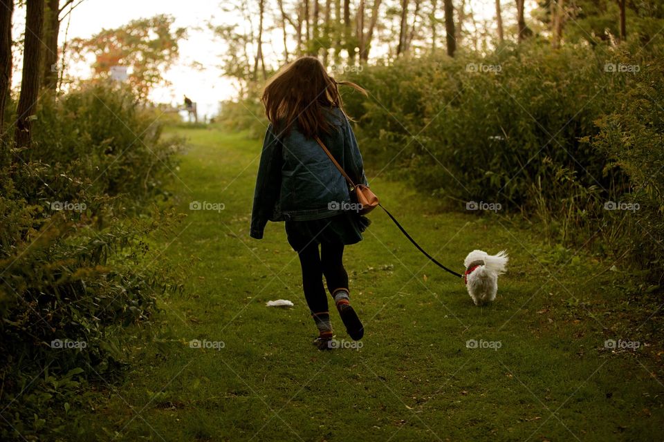 Girl walking her puppy into a forest at sunset