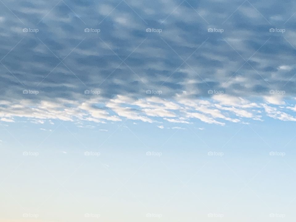 Striated colors of clear blue sky underneath popcorn clouds 