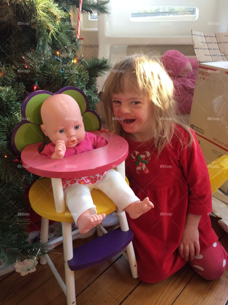 Young girl with Down syndrome playing with doll she got for Christmas by Christmas tree