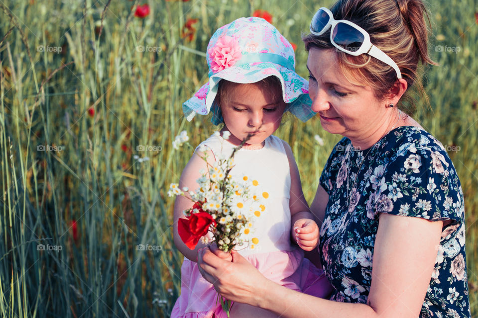 Mother and her little daughter in the field of wild flowers. Little girl picking the spring flowers for her mom for Mother's Day in the meadow. Nature scene, family time