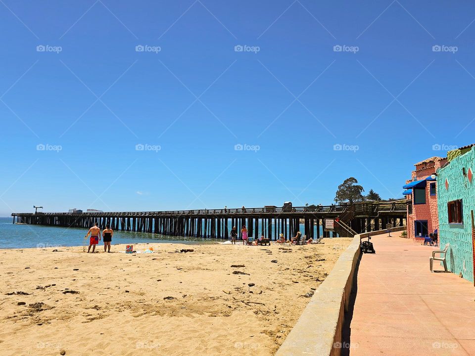 beautiful sunny summer day on the beach in Capitola california looking at the wharf down the promenade of the historic colorful Venetian hotel and condominiums with a family enjoying the clear blue sky