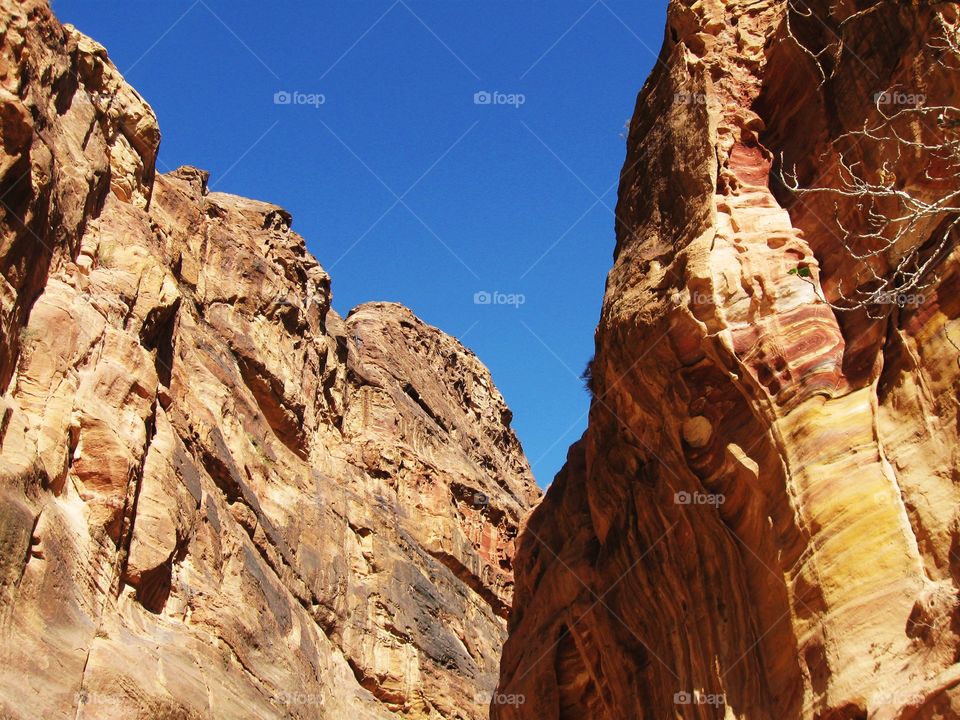 A piece of clear blue sky between two rocks in a canyon. fair weather sky on a sunny day above orange pink rocks. bright blue sky contrasting orange pink rocks