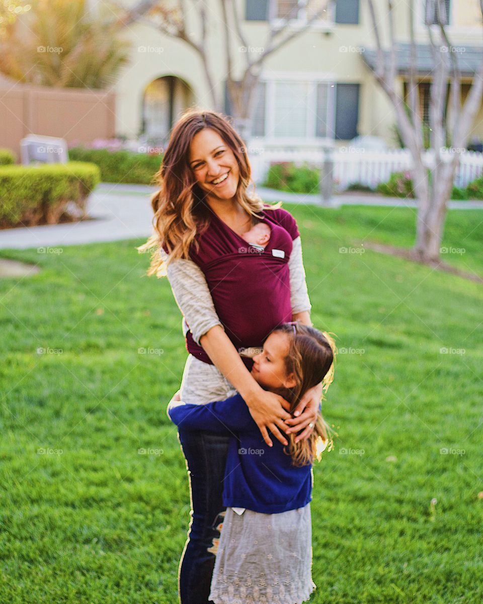 Mother loving her wrapped baby and hugging her daughter 