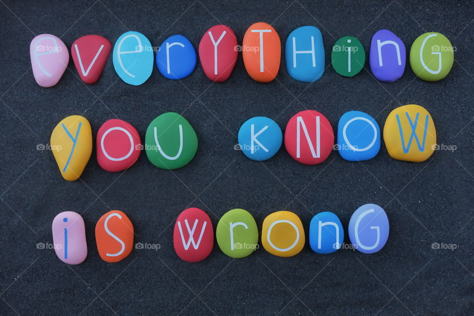 Everything you know is wrong, creative text composed with multi colored stone letters over black sand