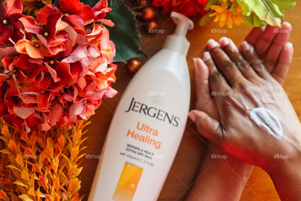 Woman applying Jergens Ultra Healing Lotion on wood background with flowers. 