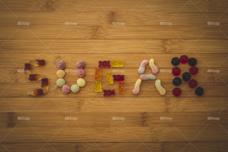 The word sugar spelled with different kinds of candy on a wooden table. it is very sweet and delicious but also unhealthy and bad for your teeth.