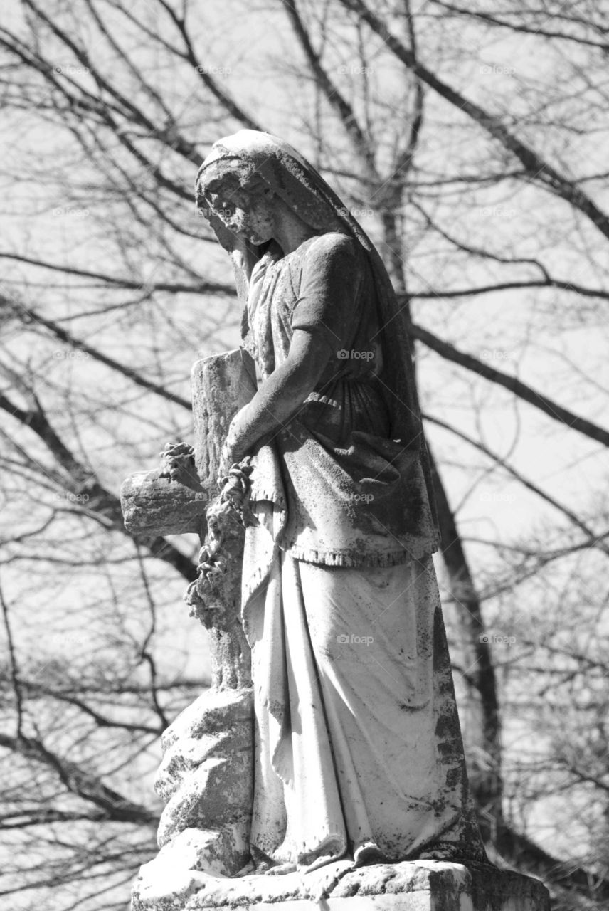 Ghostly statue holding cross shot in black and white .