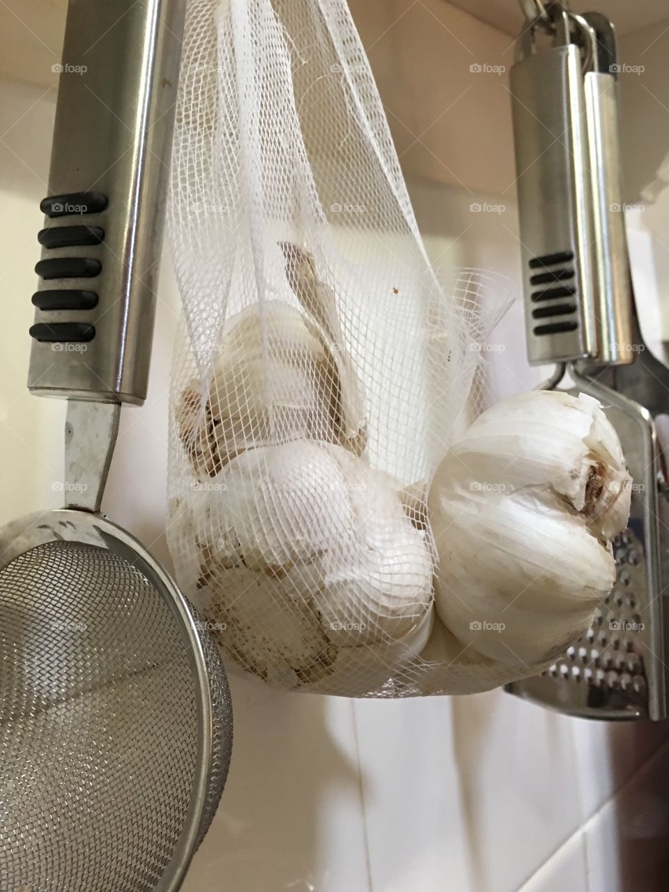 Garlic bulbs hanging in net on kitchen utensil hook