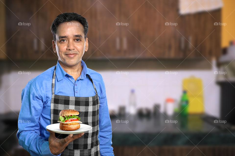 Indian chef / cook with a burger in kitchen