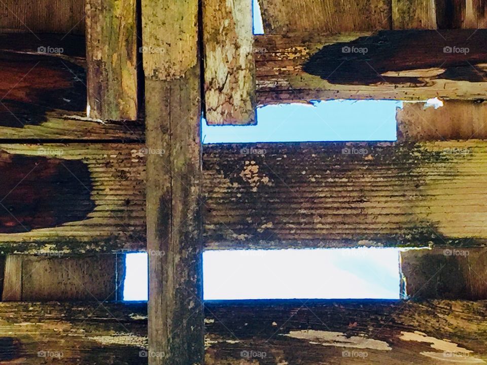 A view of bright blue sky seen through the wooden rafters of an old structure