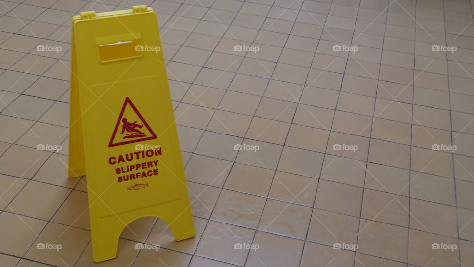 caution slippery surface yellow sign on a brown tiled floor.  with copy space.