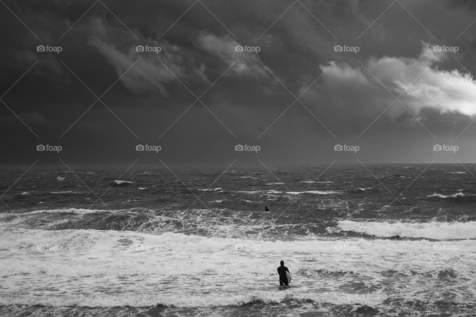 Amidst the bluster of a tempest two lone people venture fearlessly into the roaring sea to happily bob on the waves like corks. 