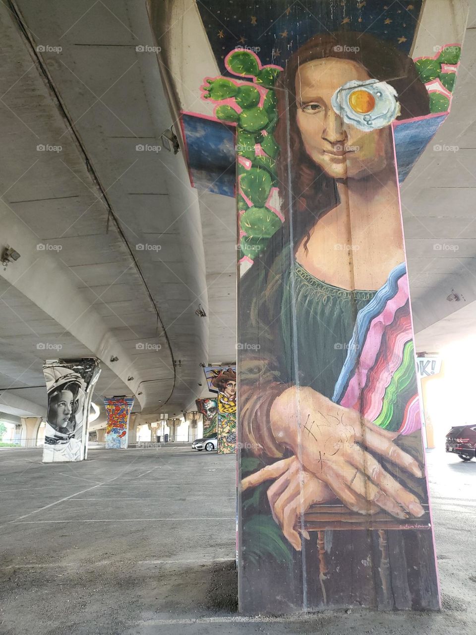 Street art on cement pillar of a highway underpass of a cultural version of what appears to be Mona Lisa.