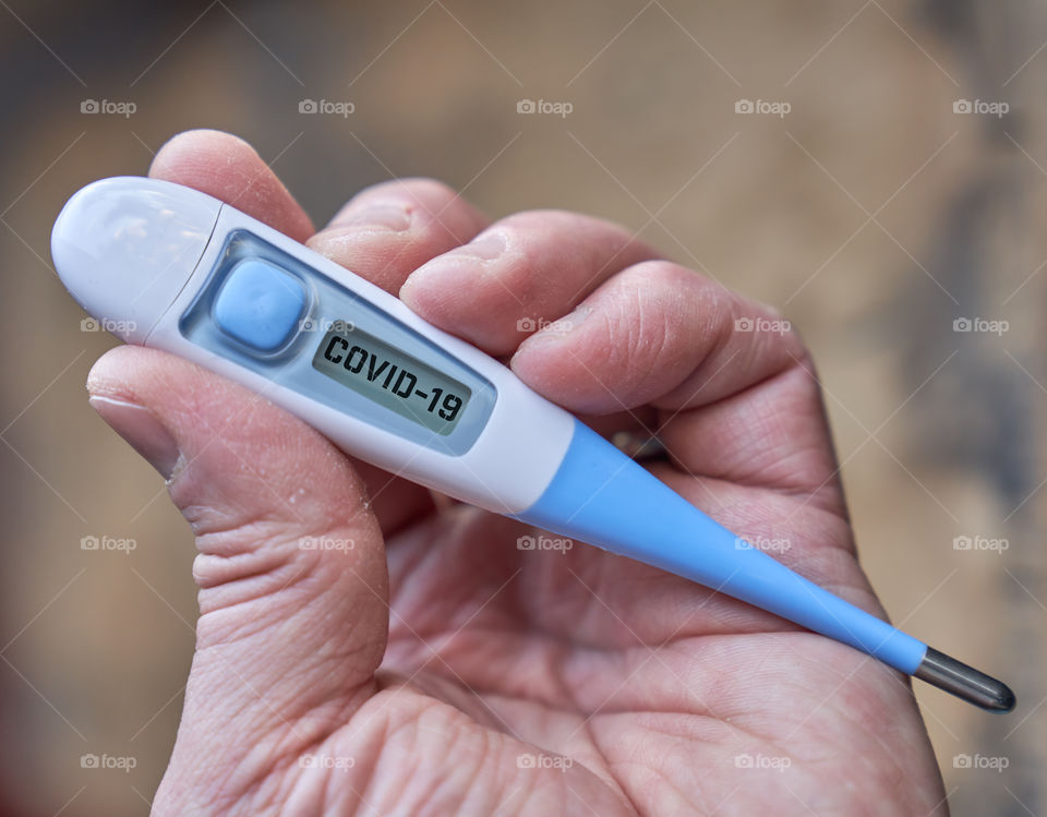 Male hand holds clinical thermometer with covid-19 text on the screen during global covid-19 or corona pandemic.