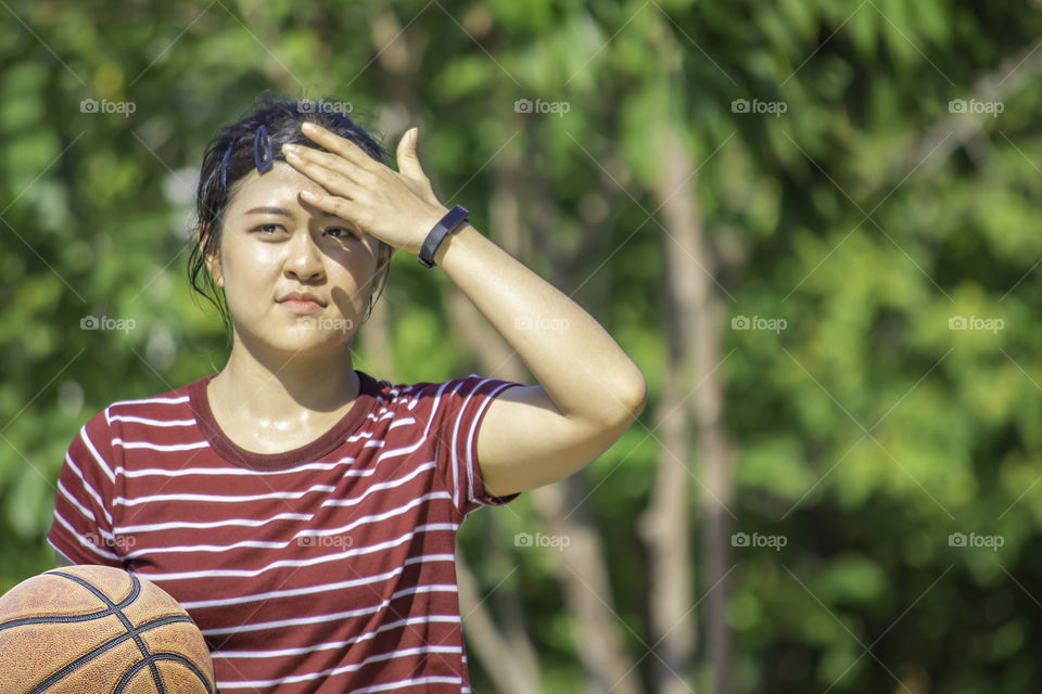 Leather basketball in hand of a woman wearing a watch Background blur tree in park.