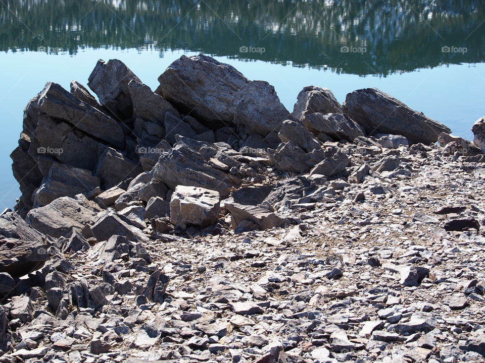 Jagged rocks and boulders along the shoreline of Ochoco Lake in Central Oregon on a sunny spring day.