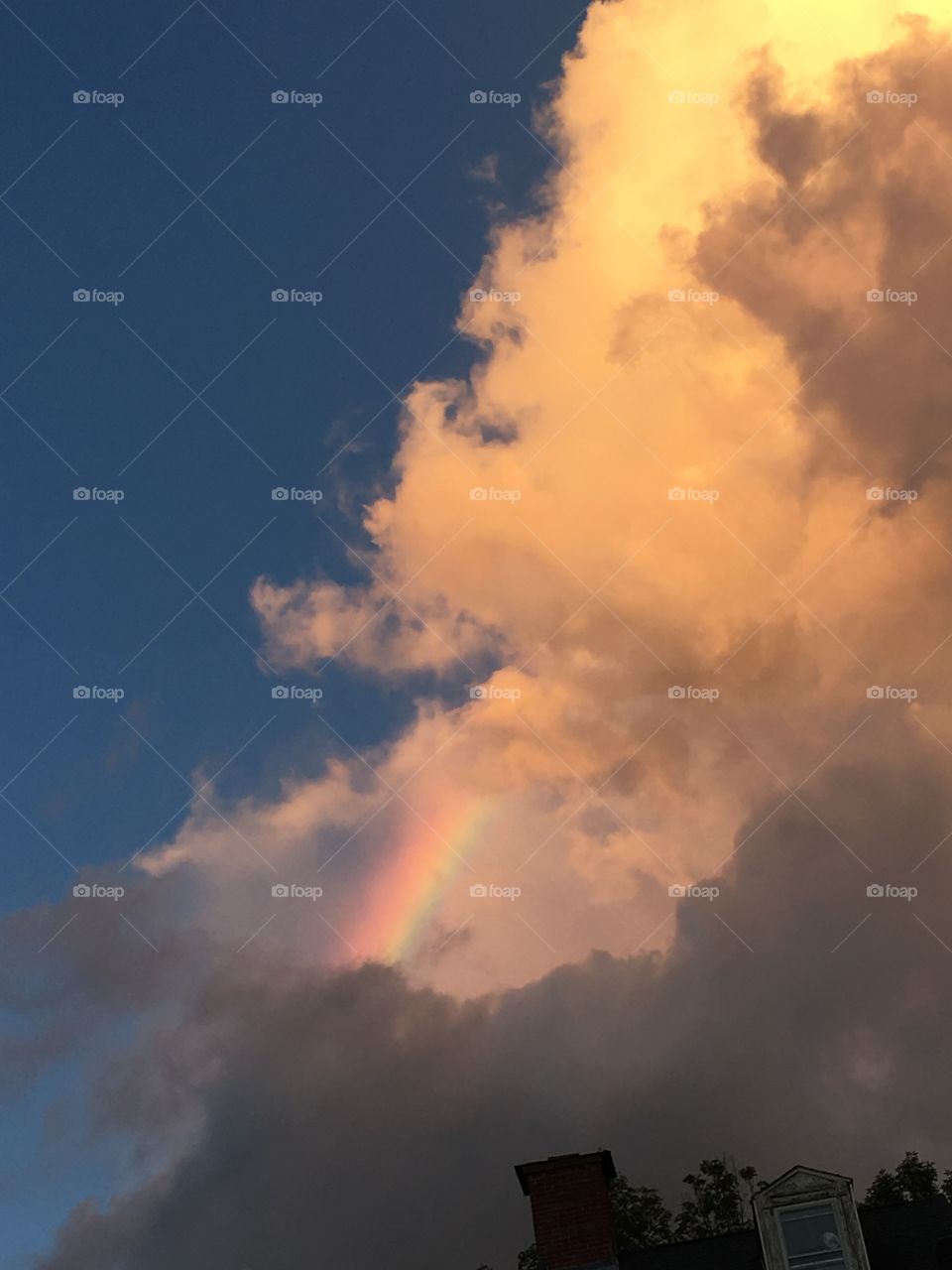 Rainbow hidden in between the clouds after rainstorm. Clouds look like smoke trying to eat it.