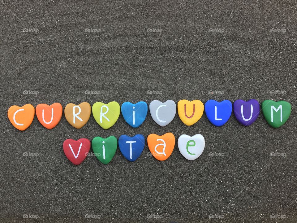 Curriculum Vitae text with colored heart stones letters over black volcanic sand