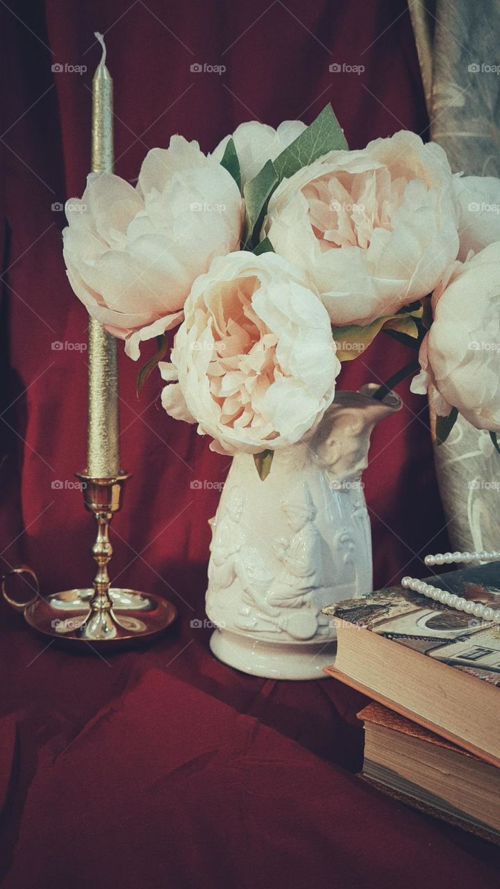 Vintage composition, flowers in ceramic vase, book and candle 