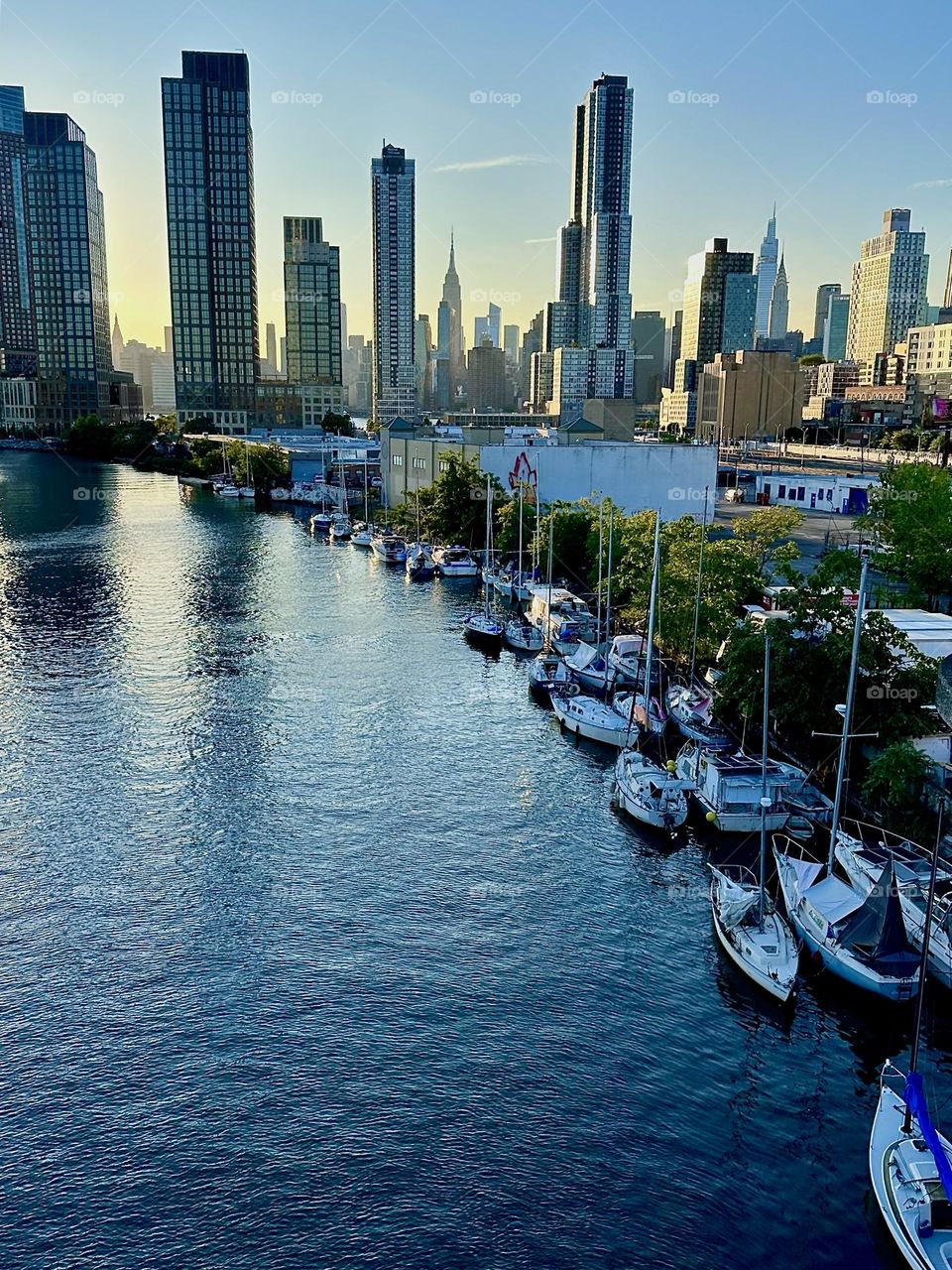 This is “Newtown Creek”, ocean inlet of the “E River” with its various kinds of boats seen from the “Pulaski Bridge” that connects “Greenpoint”, Bklyn to LIC.  In the distance we see “Manhattan” and the “Empire State Bldg”. 2024. Hypnotic Productions