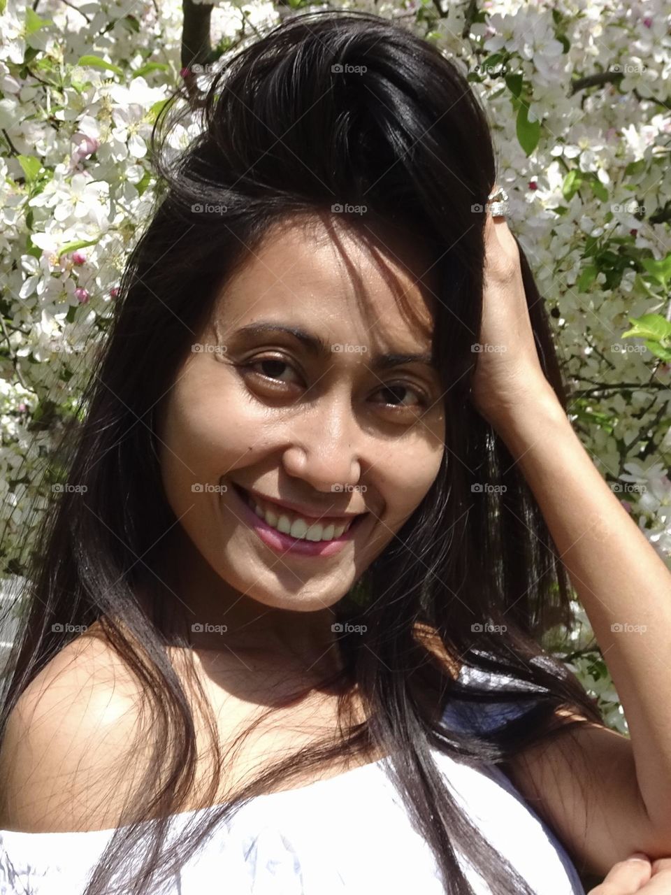 Portrait of young woman, no make up, with smiling expression and with black hair on a sunny day spring Central Park.