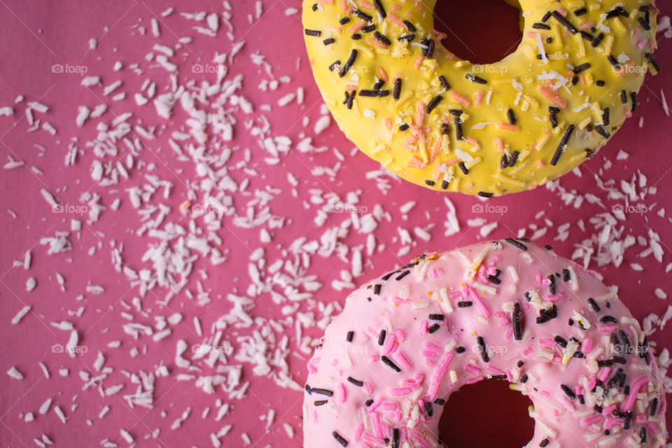 Tasty sweet yellow and pink donuts with chocolate sprinkles on the pink background with coconut flakes.