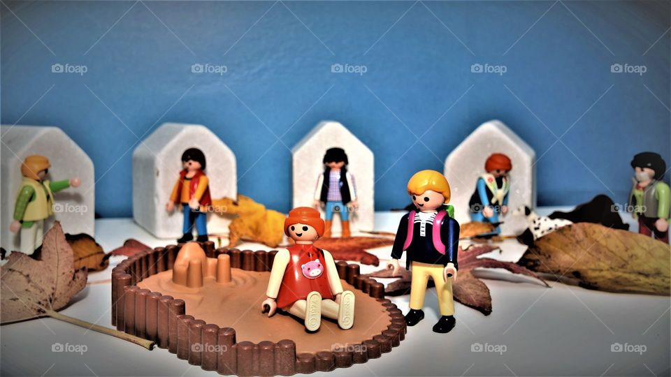 Playmobil children playing in the sand during corona lockdown with the adults staying at home or wearing a facemask