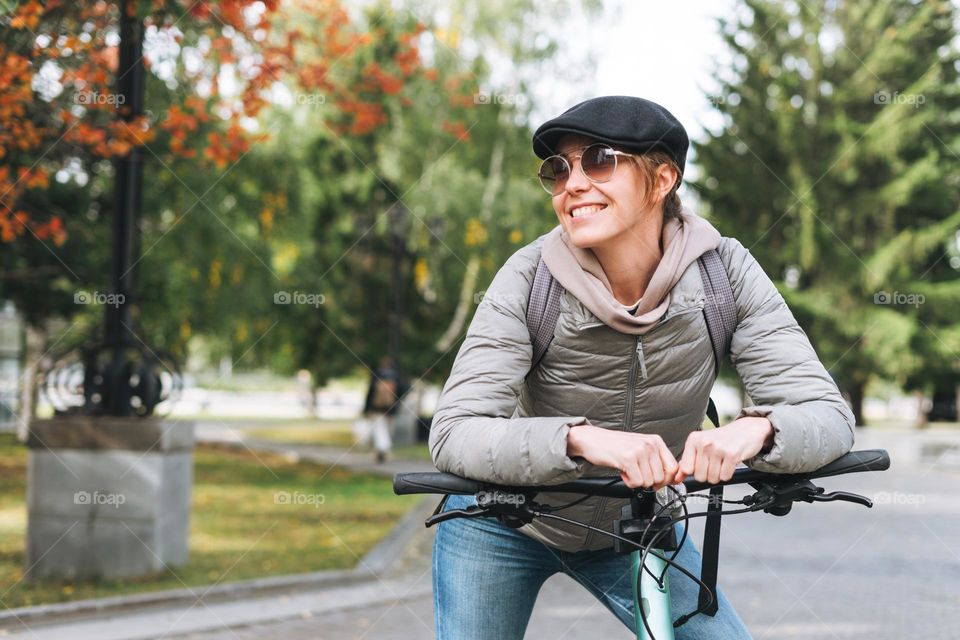 Portrait of fashionable young pretty woman in cap and sunglasses on bicycle on sunny autumn day in city park