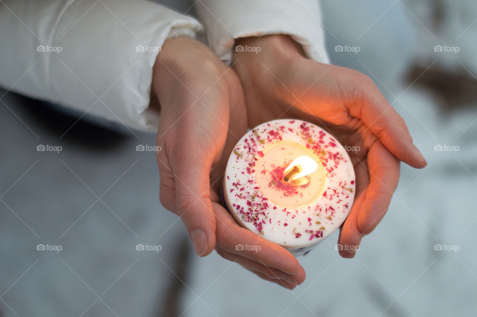 Human hands holding a burning tealight with red petals decoration