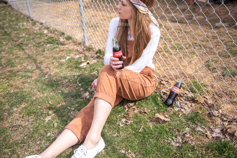 Young millennial woman sitting in the grass and holding a bottle of Coca-cola