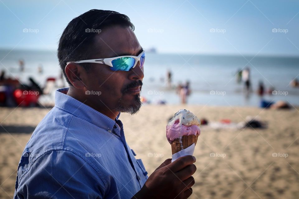 Bearded man in his 50th is eating an ice cream on a beach