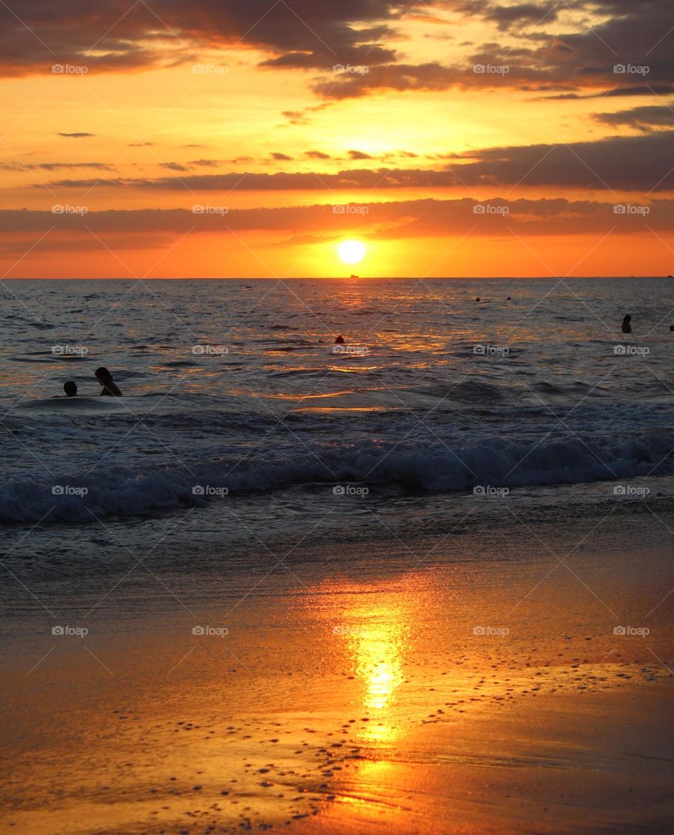 Magical sunset on the Pacific ocean.  The reflection of the sun on the sand and the silhouette of bathers