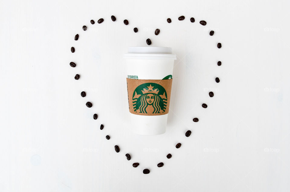 A Starbucks coffee cup laid out on a white table and surrounded by coffee beans in the shape of a heart