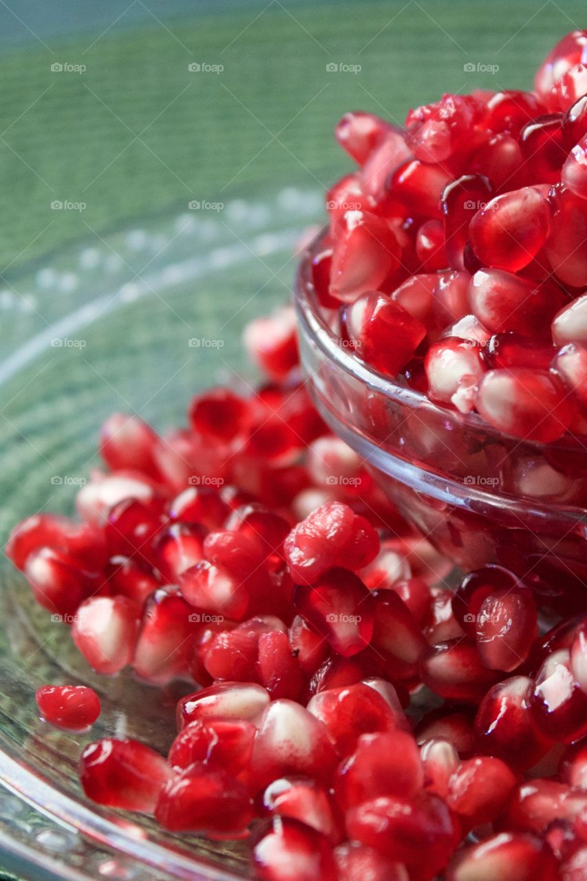 Fruits! - Closeup of fresh pomegranate seeds overflowing a small glass bowl against a green background