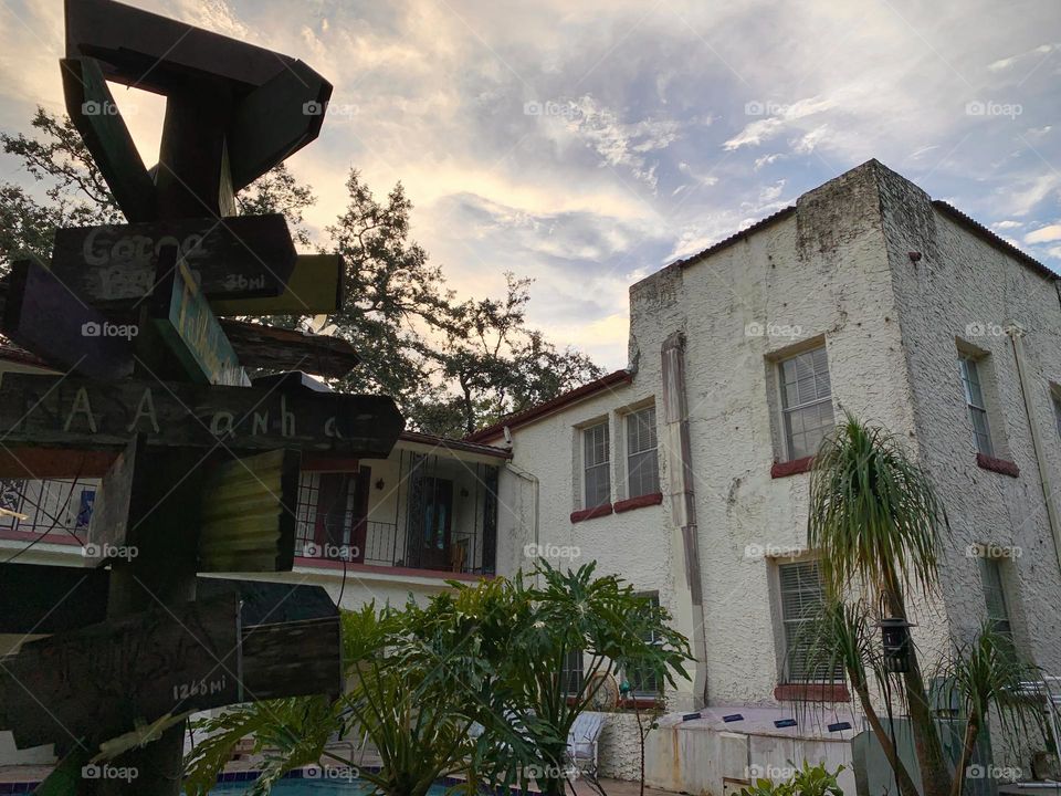 White and red spanish old style architecture residential large house built in the early 1900s. Many windows on the side of the house with aging signs with charming pretty style and beautiful landscaping with pool, chairs, focus on destinations arrows