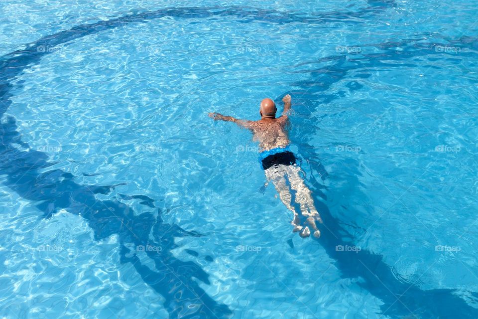 Senior man swims in the pool, view from above