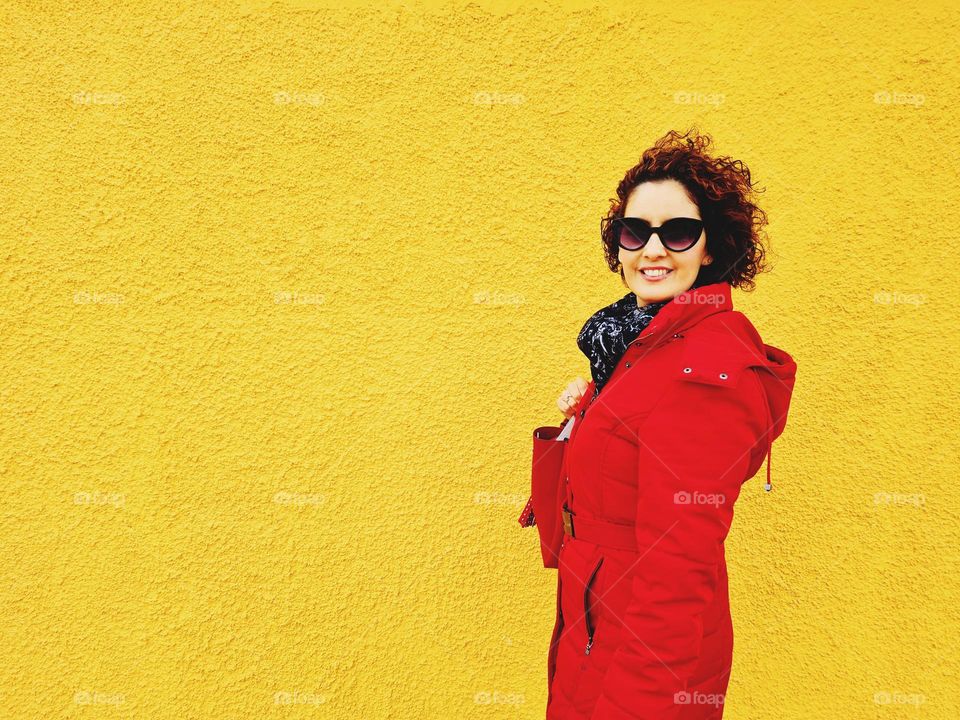 smiling woman with red jacket in front of a yellow wall