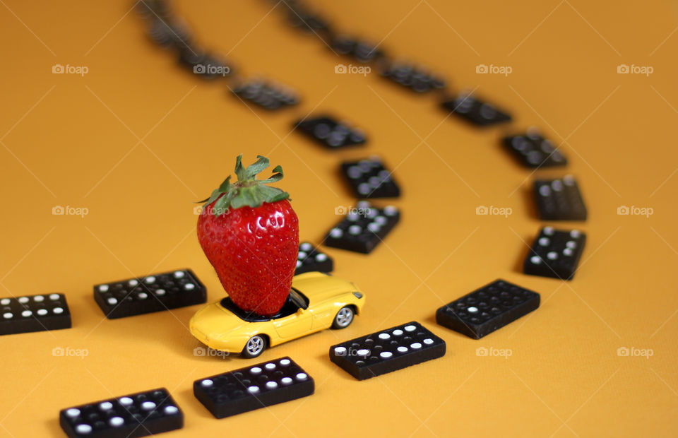 Still life, strawberry in a toy car and domino pieces road