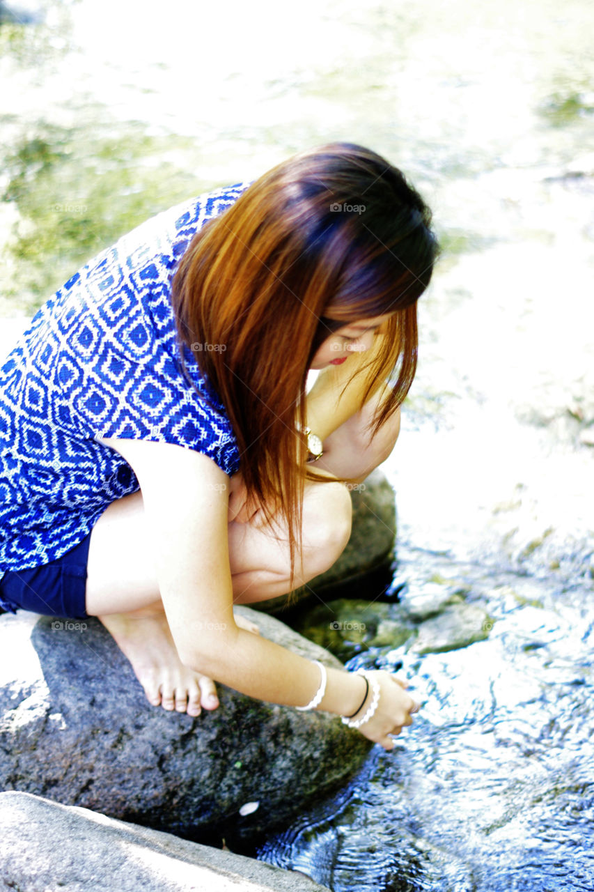 Girl in blue dress touching creek water