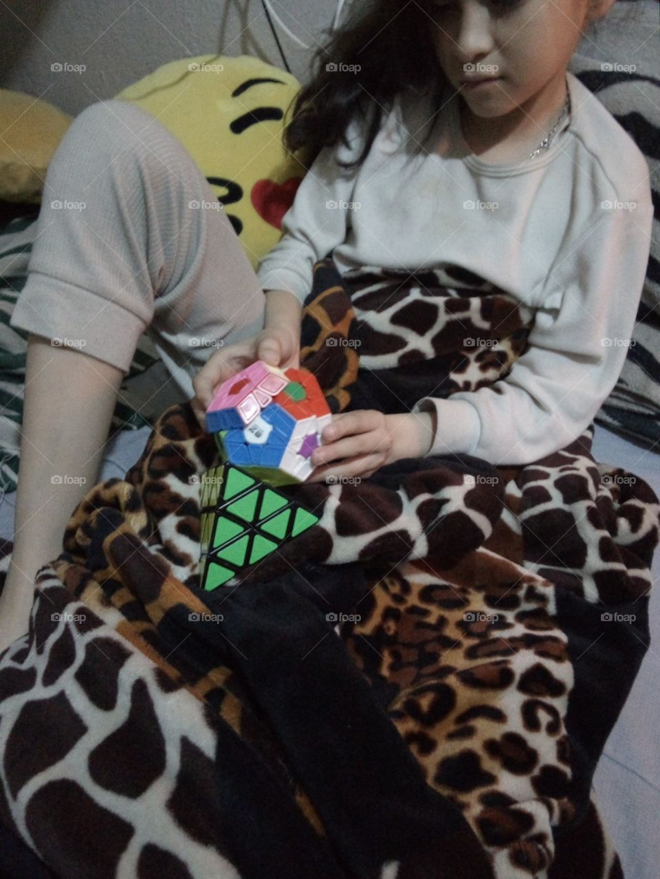 niña jugando cubo Rubik de varias formas y colores tapada con cobija mientras hace frío... en pijama.