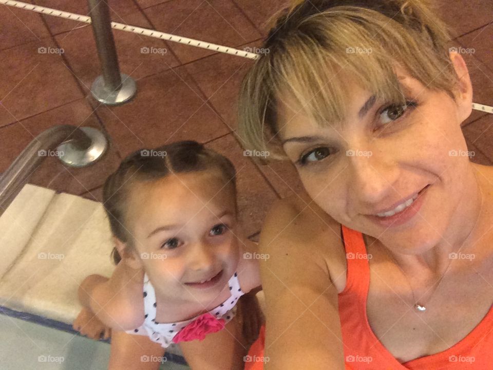 Poolside Pose. Young mother and toddler girl sitting on the edge of an indoor pool in a hotel. 
