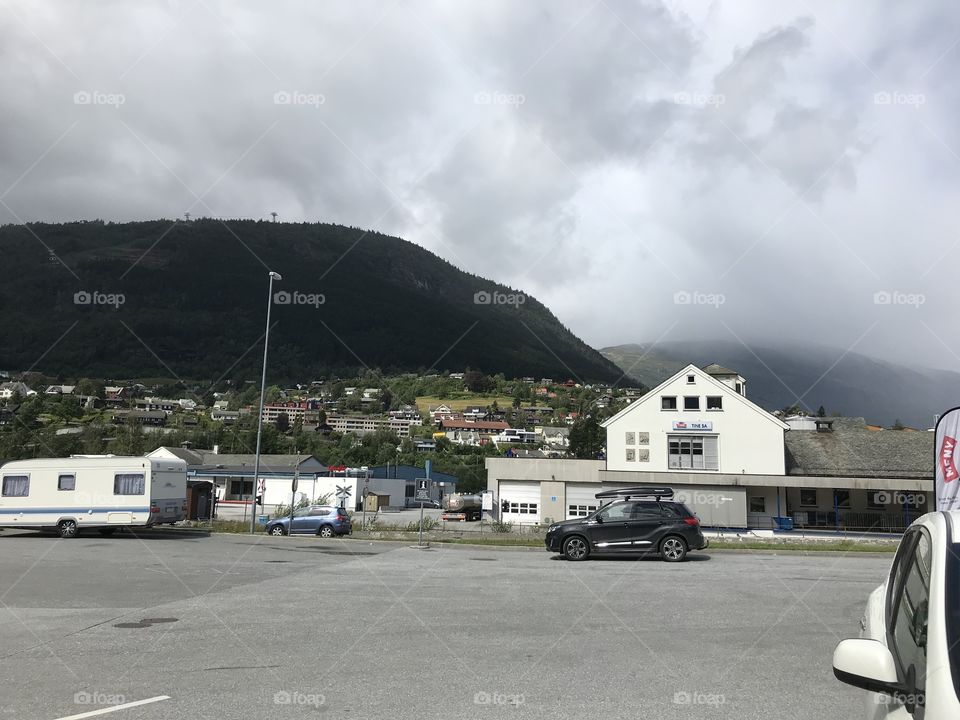 One car in front of a shop in Norway. The car is black and the shop is white. It’s a mountain behind it.