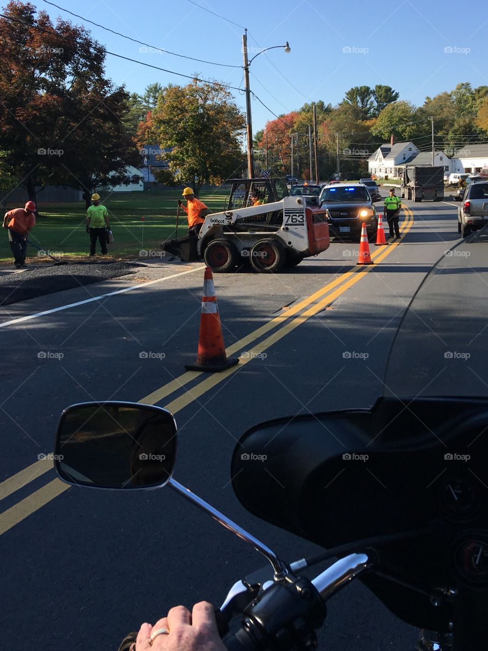 Road construction, machinery, men working, policeman & vehicle causing us a traffic jam.