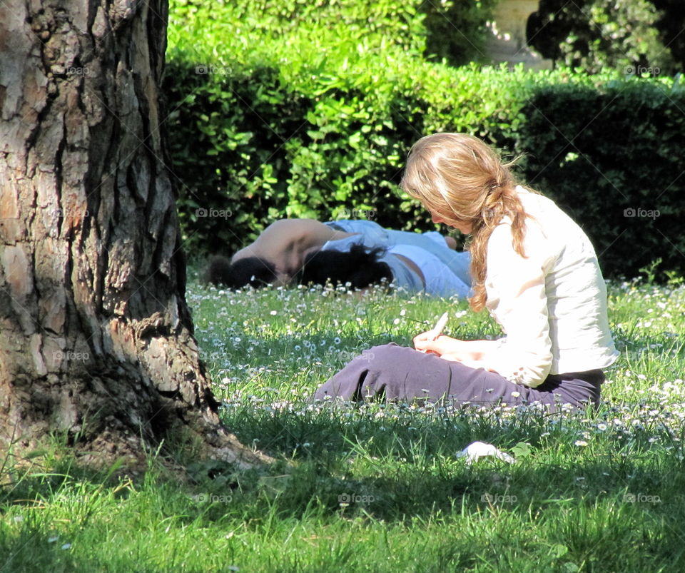 blonde young girl learning and studying in a green garden