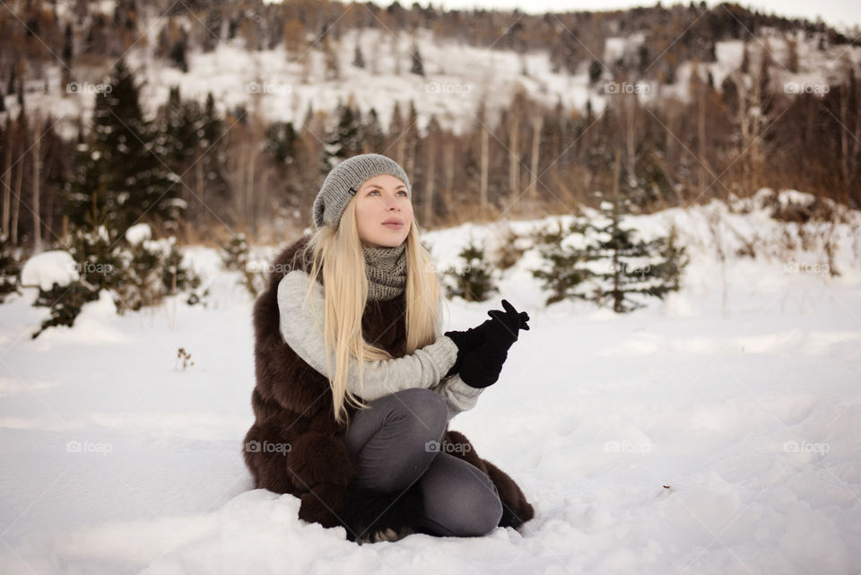 Beautiful blonde woman sitting on snowy landscape